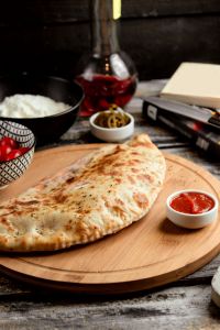 pizza calzone on wooden board _ | Plum Tomatoes Brick Oven Pizza